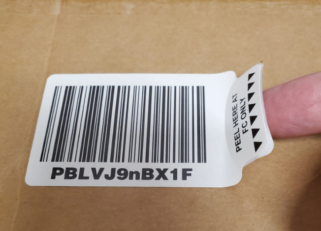 finger lifting up tab side of Clean Tac label showing a barcode